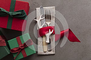 Christmas day table setting with cutlery wrapped in a red ribbon and gift box presents