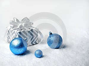 Christmas decor. Blue Christmas balls and gift box with white bow, on white snow