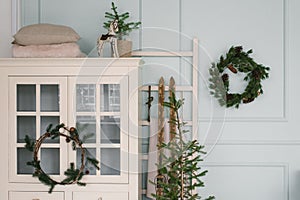 Christmas decor in the interior of the room. Christmas tree, wreath and white wardrobe in blue and white tones