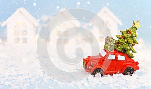 Christmas decor - red retro car on snow carries past white houses with lights garlands in bokeh Christmas tree with gift boxes on