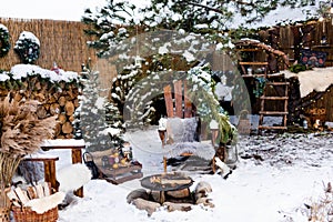 Christmas decor in the yard: a Christmas tree with a garland, wooden chairs by the fire, firewood,