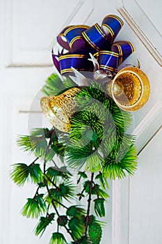 Christmas decoration with accented ribbon, golden bell, and plastic pine leaves mounted in front of white door