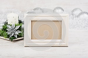 Christmas decoration with candle and empty photo frame on white wooden background. White frame mock-up