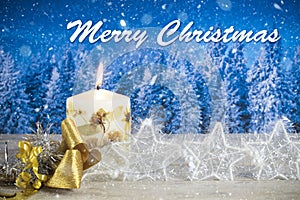 Christmas decoration with candle, golden bow, silver stars, with text in English `Merry Christmas` in a blue forest background