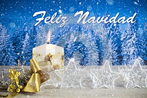 Christmas decoration with candle, golden bow, silver stars, with text in Spanish `Feliz Navidad` in a blue forest background