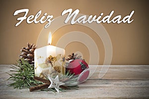 Christmas decoration with candle, pine, bauble, with text in Spanish `Feliz Navidad` in wooden background