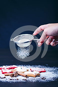 Christmas decoration and cookies.Woman hand sprinkling sugar on a cookies. Flour and spices for a baking on a dark backg