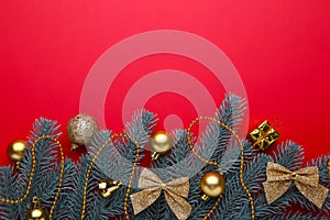 Christmas decoration. Fir-tree branch with gold balls, little gifts and bows on a red background