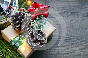 Christmas decoration with fir tree,gift box,red berries,garland lights and pine cones on old wooden background.