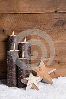 Christmas decoration: Four burning candles, stars and snow on wooden background