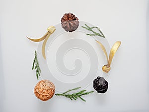 Christmas decoration or ornament laid in circle frame composed of green pine branch, brown pine cone, brown and black wooden ball,