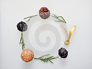 Christmas decoration or ornament laid in circle frame composed of green pine branch, brown pine cone, brown and black wooden ball,