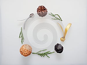 Christmas decoration or ornament laid in circle frame composed of green pine branch, brown pine cone, brown and black wooden ball,