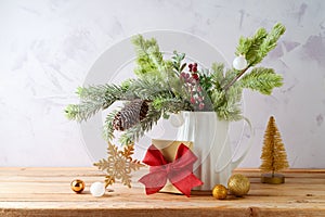 Christmas decoration with pine tree branches in vase, gift box  and golden ornaments on wooden table over bright background