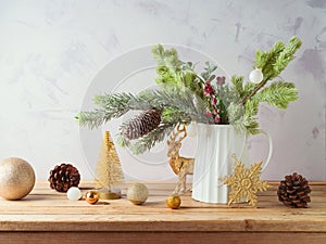 Christmas decoration with pine tree branches in vase and golden ornaments on wooden table over bright background