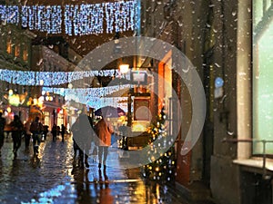 Christmas decoration in rainy city street ,people walking,romantic senior couple under umbrellas in Tallinn old town evening blurr