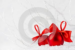 Christmas decoration - two rich red glossy glitter balls with satin ribbon in decorative soft light white winter forest with frost