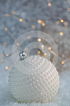 Christmas decoration. White ball nacre pearls on a snow and beautiful blurred background of glittering bokeh with glowing lights.