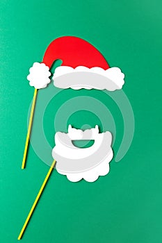 Christmas decoration, white beard and red Santas hat on sticks. Festive concept, party accessories. Vertical, flat lay. Minimal