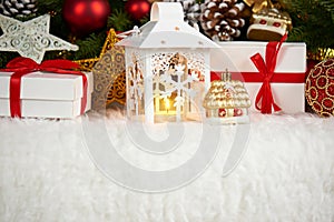 Christmas decoration on white fur with fir tree branch closeup, gifts, xmas ball, cone and other object on dark background with li