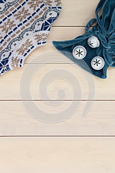 Christmas decoration wooden background with knitted wool sweater with jacquard ornament, blue velvet bag with bells snowflakes.