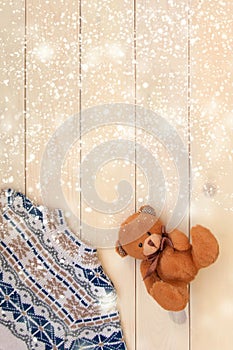 Christmas decoration wooden background with knitted wool sweater with jacquard ornament in white blue and beige. brown bear toy.