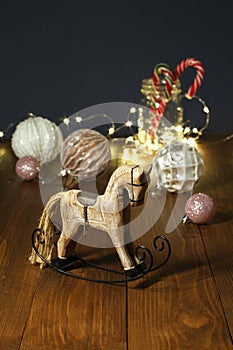 Christmas decoration - wooden toy rocking horse, balls for the Christmas tree, New Year`s candies in a glass jar, with garland