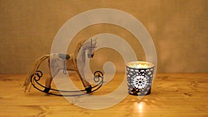 Christmas decoration - wooden toy rocking-horse and candle in candlestick on wooden table against concrete wall. Closeup