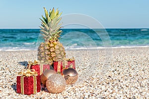 Christmas decorations, baubles and pineapple on a sandy beach on a bright and sunny day. New Year concept