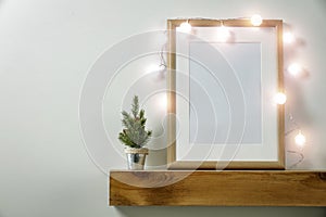 Christmas decorations in bright shiny colors with Christmas lights and frame picture. Wooden shelf and white wall background.