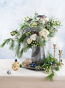 Christmas decorations, candles and flower bouquet. Winter arrangement with roses, fir branches, winter berries. Christmas flower