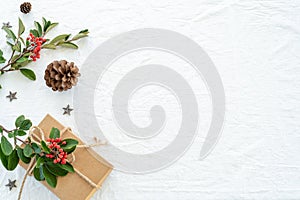 Christmas decorations composition on white linen background with gift box, pine branches, pine cone, wooden stars and red berry