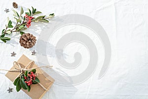 Christmas decorations composition on white linen background with gift box, pine branches, pine cone, wooden stars and red berry