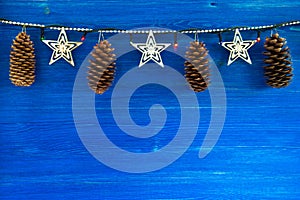Christmas decorations with cones and Christmas lights on the blue wooden background.
