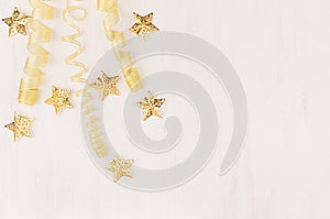 Christmas decorations, curl ribbon and gold stars falling on soft white wooden background.