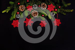 Christmas decorations, fir branches, cones and knitted snowflakes on a black background