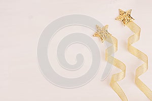 Christmas decorations, firework of gold stars and curl ribbon on soft white wooden background.