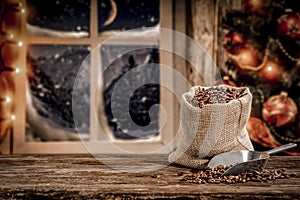 Christmas decorations and fresh coffee beans in jute sack with blurred christmas tree and night window background.