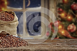 Christmas decorations and fresh coffee beans in jute sack with blurred christmas tree and sowy night window background.