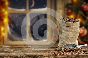 Christmas decorations and fresh coffee beans in jute sack with blurred christmas tree and sowy night window background.