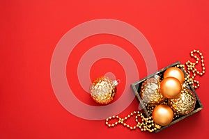 Christmas decorations. Gold baubles and beads in the wooden box on the red background with copy space.