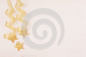 Christmas decorations, gold stars and curl ribbon on soft white wooden background.