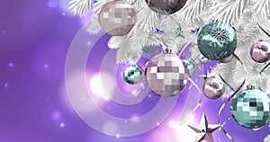 Christmas decorations hanging on christmas tree against spots of light on purple background