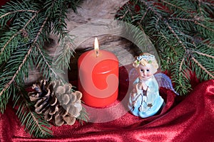 Christmas decorations with little toy angel, candle burning, cone and fir tree