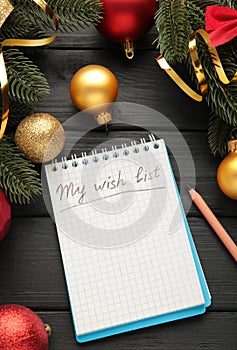 Christmas decorations and notebook with wish list on black wooden background. Planning concept