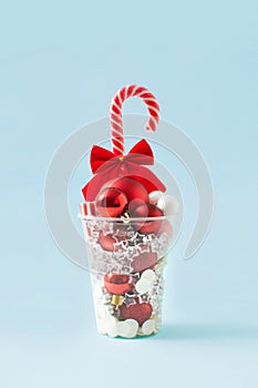Christmas decorations in a plastic cup. A metaphor for a New Year`s drink. Christmas composition minimal concept. White and red