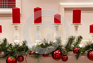 Christmas decorations and red candles stand on the fireplace