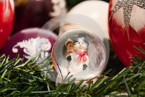 Christmas decorations. Shiny magical crystal ball with snowman and Christmas balls on tree twig. Snowing dome with xmas background