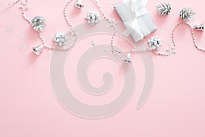 Christmas decorations, stylish silver gift box, pine cones, ribbon, confetti on pastel pink background. Minimal flat lay style photo