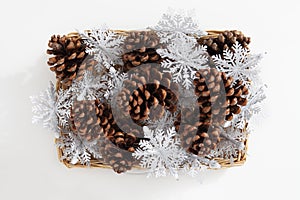 Christmas decorations, top view of a group of large pine cones and snow flake inside a wicker basket, isolated on white background